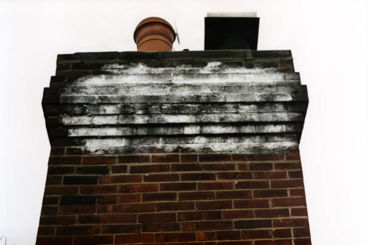 a brick chimney with white efflorescence staining on the upper courses, muted colors